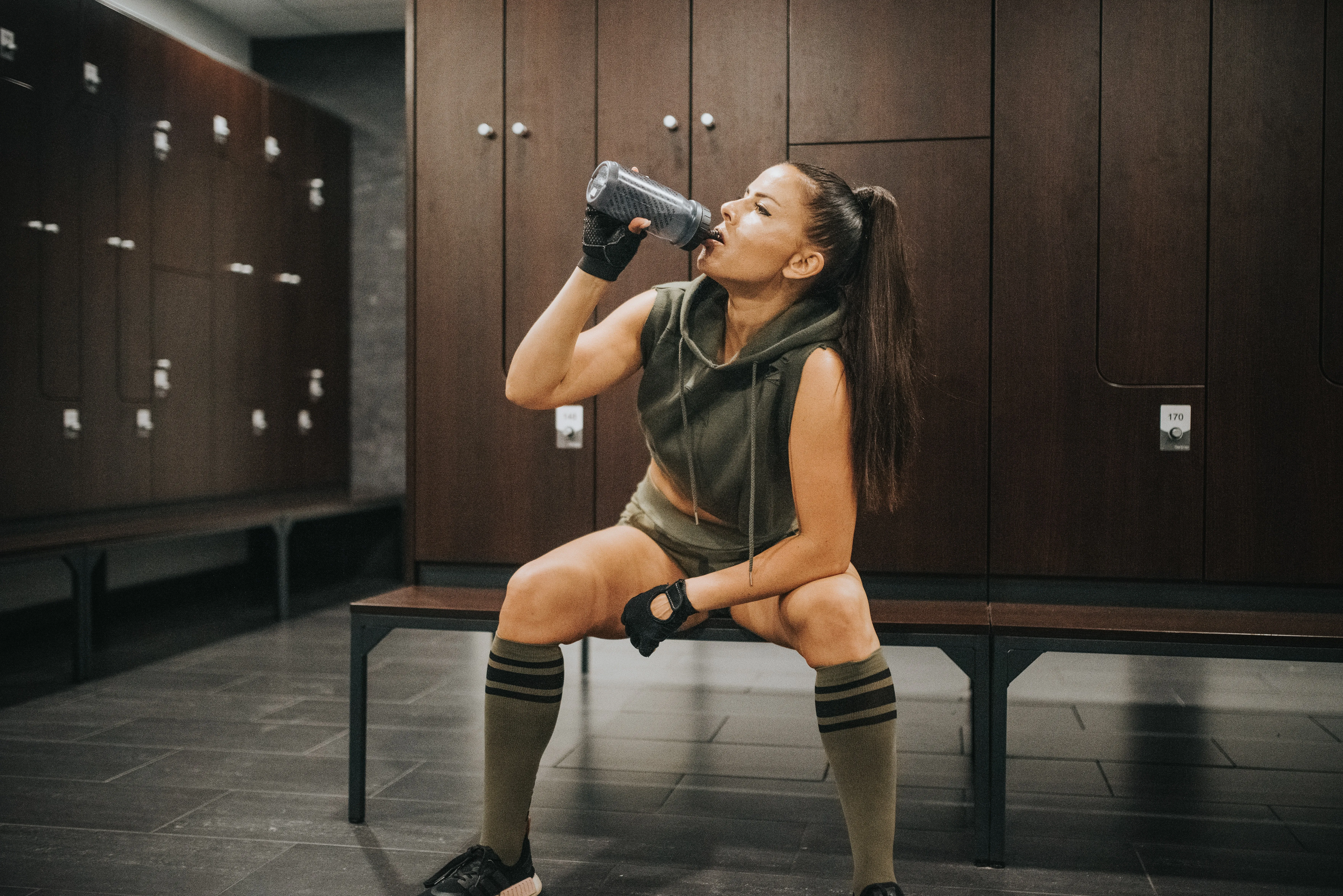 woman-drinking-from-water-bottle-in-gym-locker